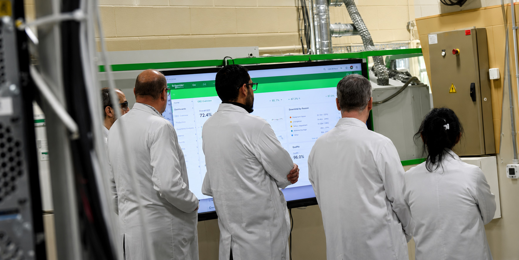 Schneider Electric team reviewing an OEE dashboard on a plant-floor display